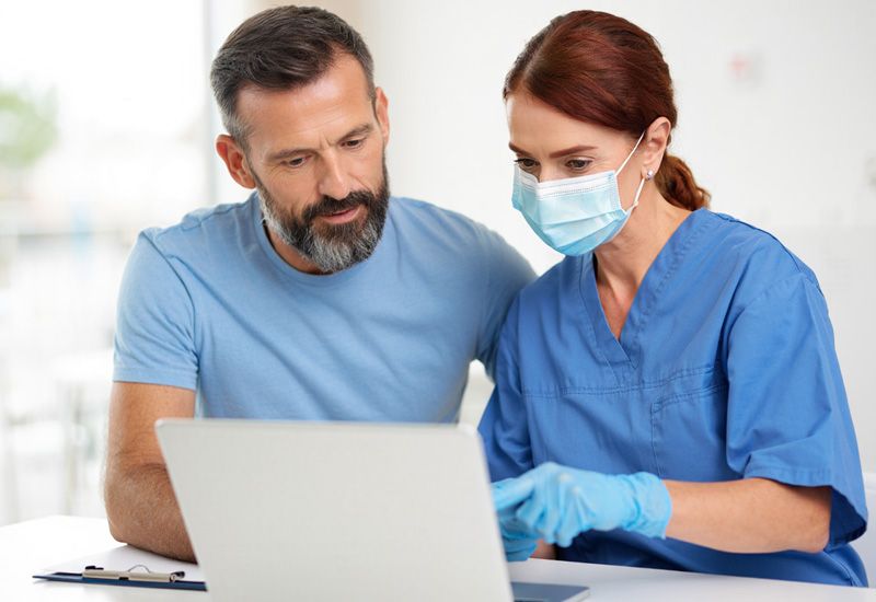 Мужчина в голубой больничной рубашке на приеме у врача перед ноутбуком